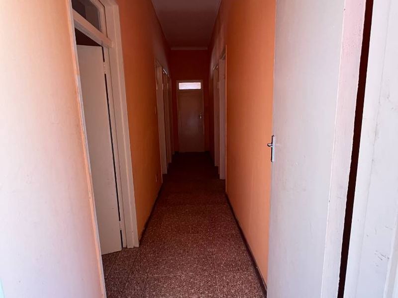 A long, empty residential hallway featuring terrazzo flooring and multiple internal doors, currently finished with dated orange wall paint.