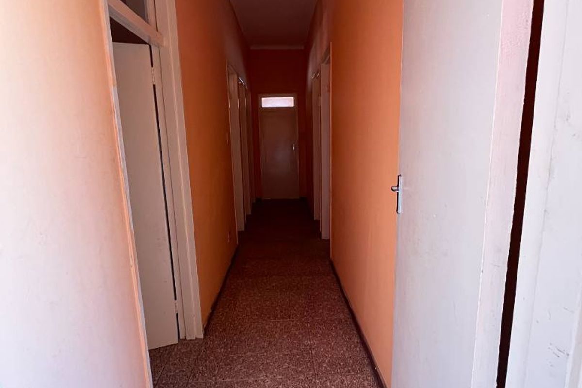 A long, empty residential hallway featuring terrazzo flooring and multiple internal doors, currently finished with dated orange wall paint.