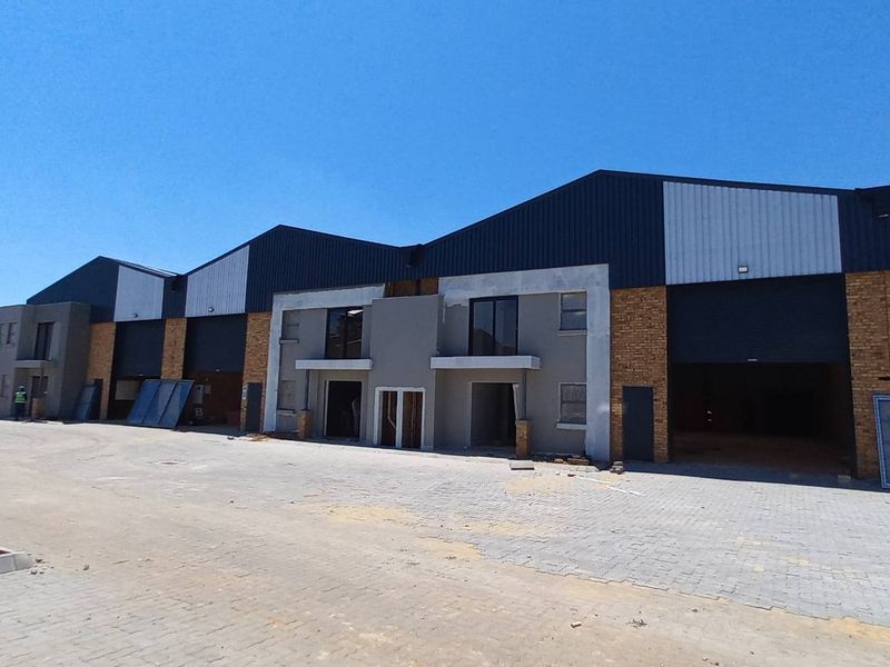 A modern industrial warehouse complex featuring multiple roller shutter doors, metal cladding, and brick facade elements with an expansive paved yard area.
