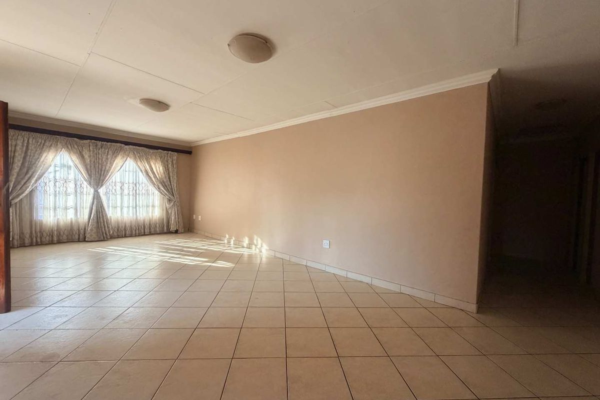 A spacious, empty living area featuring neutral tiled flooring, coved cornicing, and natural light entering through large window treatments.