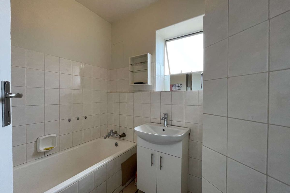 A functional bathroom featuring a white bathtub, a vanity basin with storage cabinet, and tiled walls.