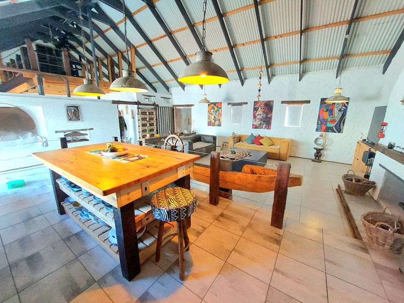 Spacious open-plan living area featuring high vaulted ceilings with exposed rafters, tiled flooring, a built-in fireplace, and a mezzanine level overlooking the space.