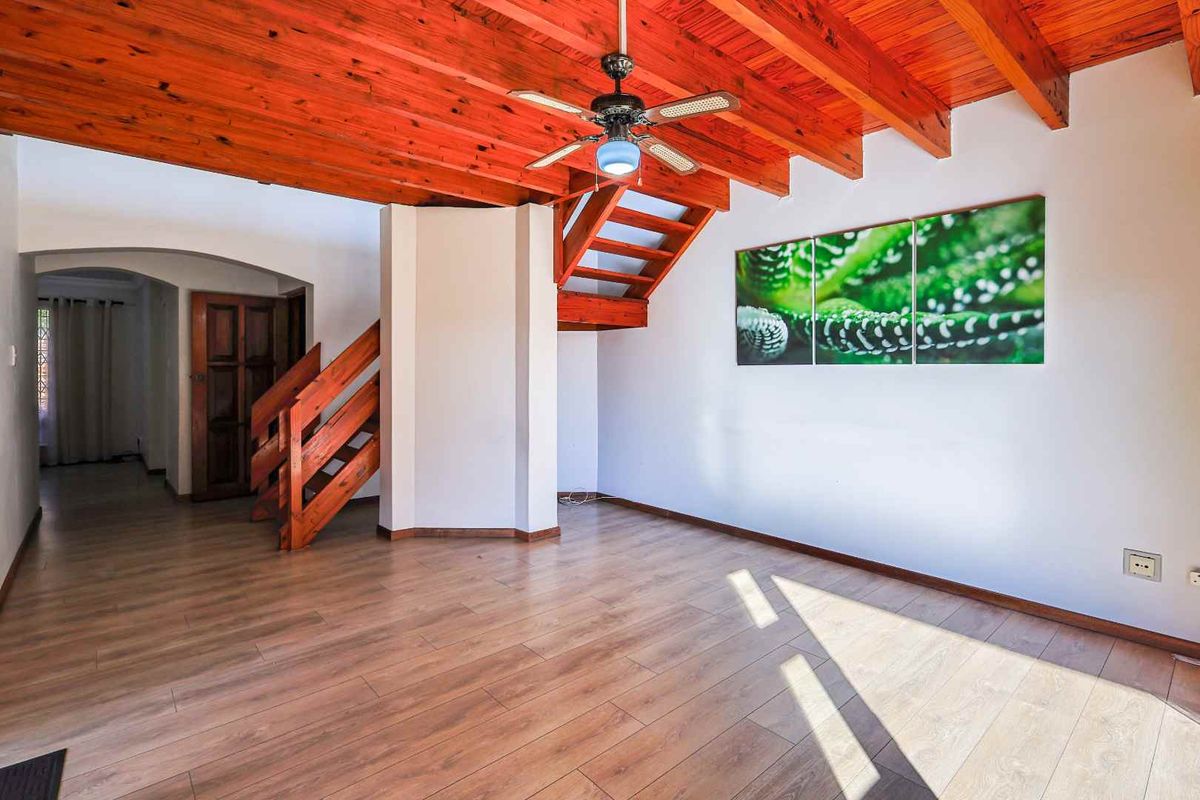 Open plan living area featuring exposed timber beam ceiling, wooden staircase, and laminate flooring, providing a warm and inviting atmosphere.