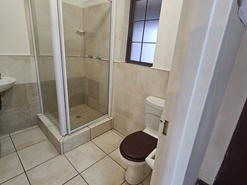 A functional bathroom featuring a shower enclosure, pedestal basin, and toilet with neutral wall and floor tiling.