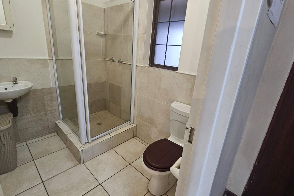 A functional bathroom featuring a shower enclosure, pedestal basin, and toilet with neutral wall and floor tiling.