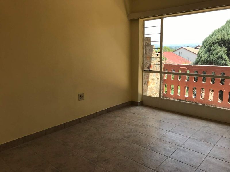 An empty bedroom featuring tiled flooring, neutral walls, and a large window providing natural light and access to an outdoor balcony area.