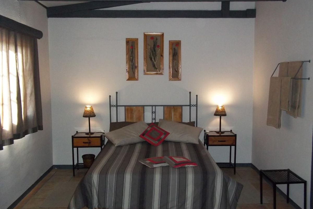 A rustic bedroom featuring exposed timber ceiling beams and tiled flooring, creating a cozy and traditional farm-style atmosphere.