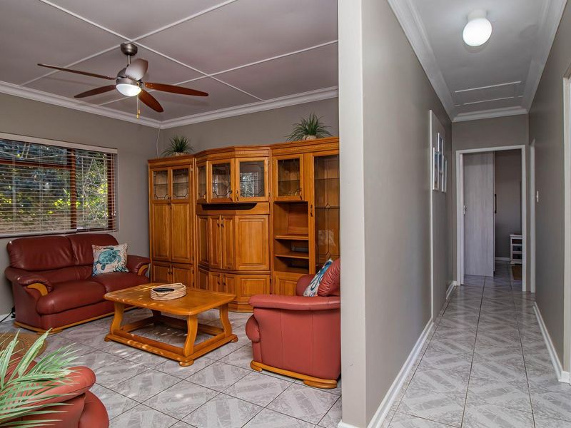 A living room featuring tiled flooring, coved cornicing, and a ceiling fan, with an adjacent hallway leading to other areas of the home.