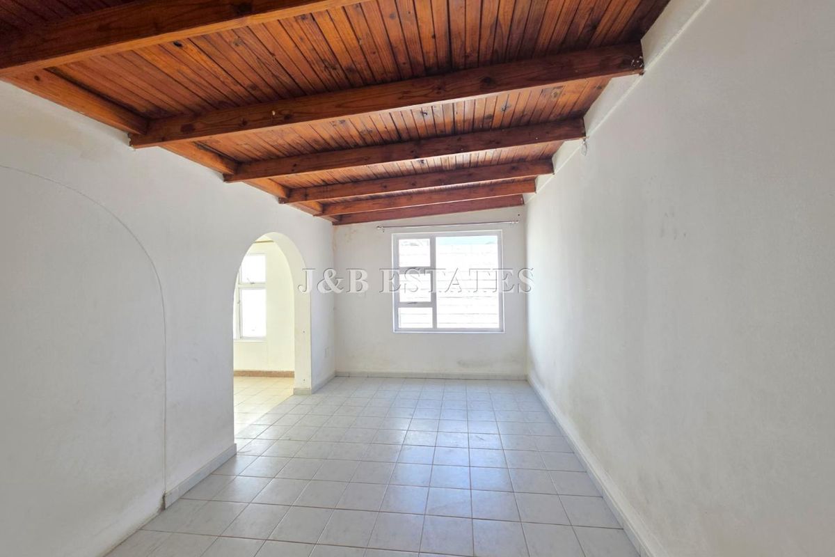 An empty living area featuring exposed timber ceiling beams, tiled flooring, and an arched doorway leading to an adjacent space.