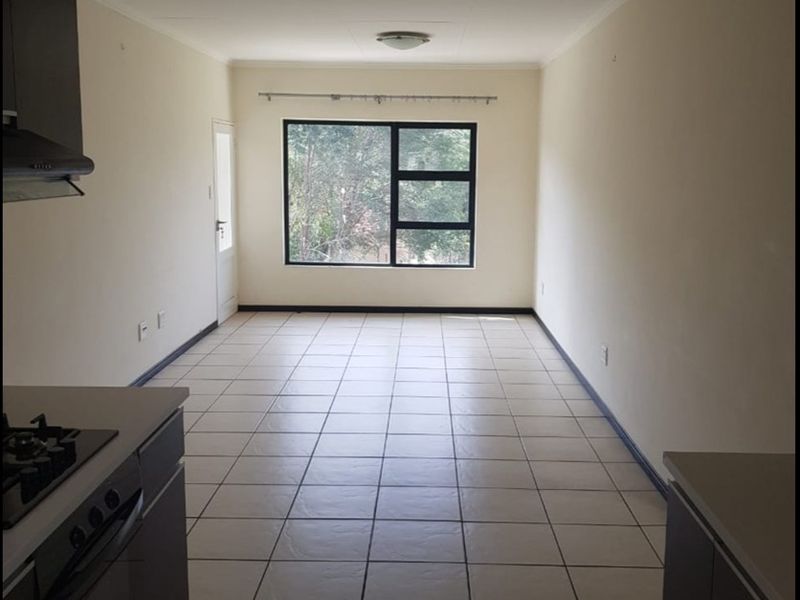 An empty open-plan living and kitchen area featuring tiled flooring, built-in cabinetry with a gas hob, and large windows providing natural light.