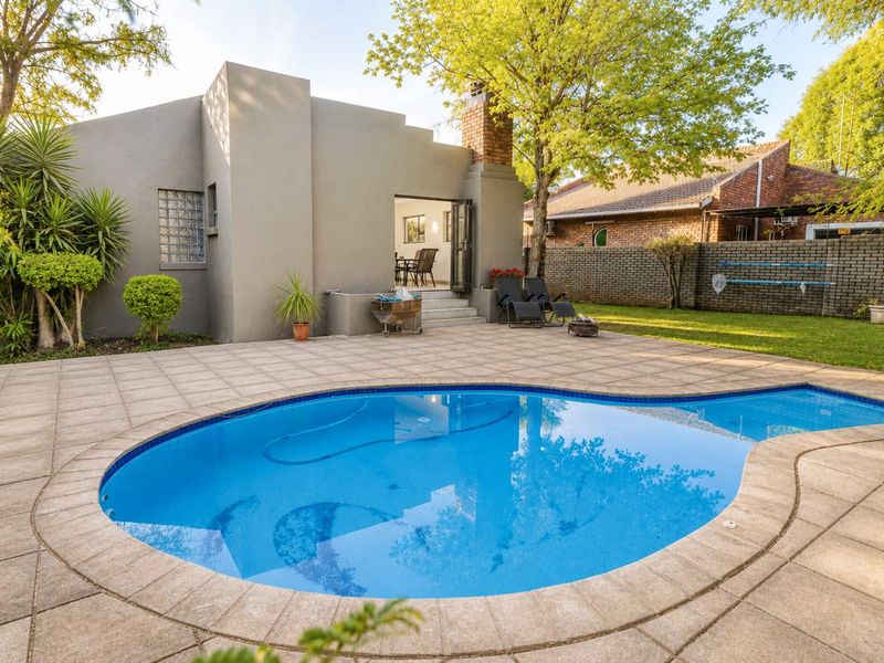 A well-maintained backyard featuring a swimming pool, paved patio area, and established garden, providing a private outdoor space for relaxation and entertainment.