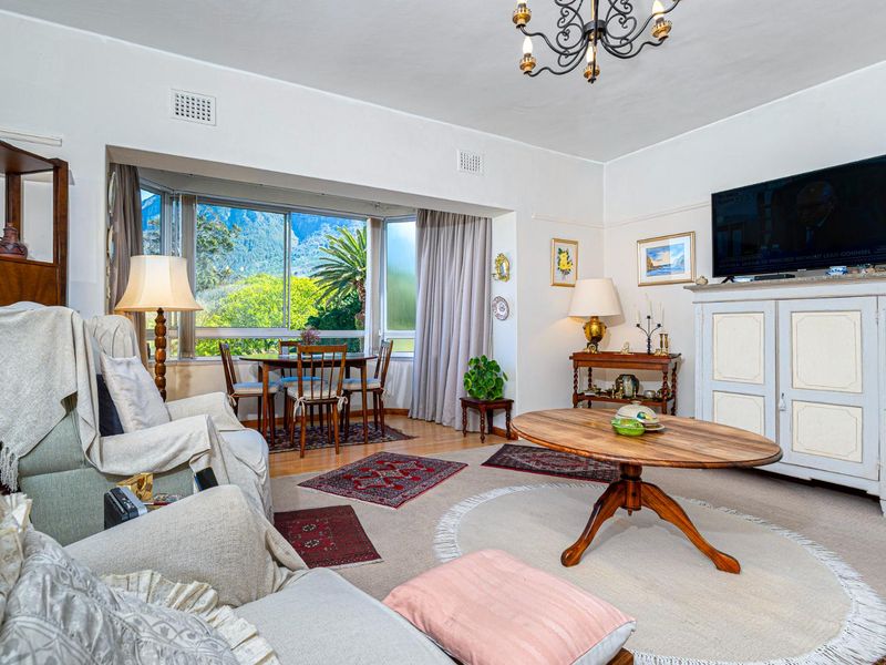A comfortable living room featuring a large bay window with scenic views, hardwood flooring, and a classic chandelier.