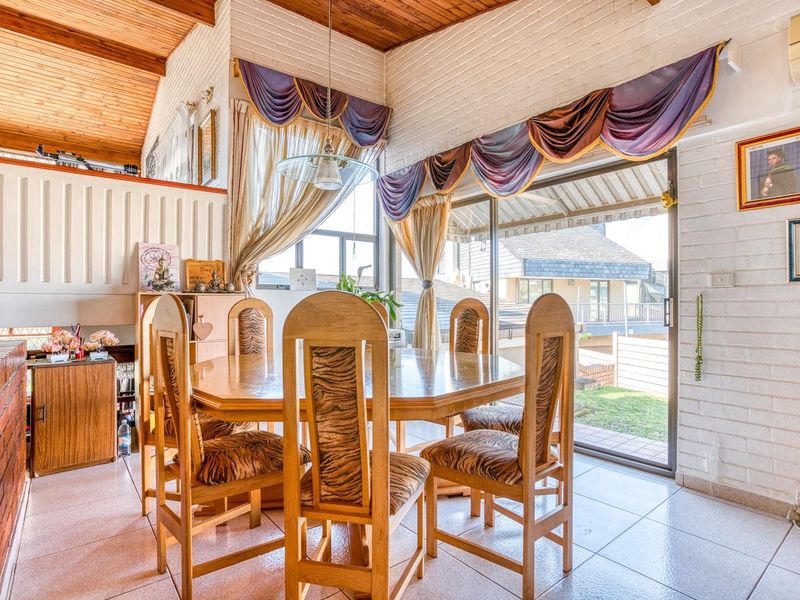 Dining area featuring a vaulted timber ceiling, exposed brick walls, tiled flooring, and direct access to the outdoor patio through a sliding glass door.