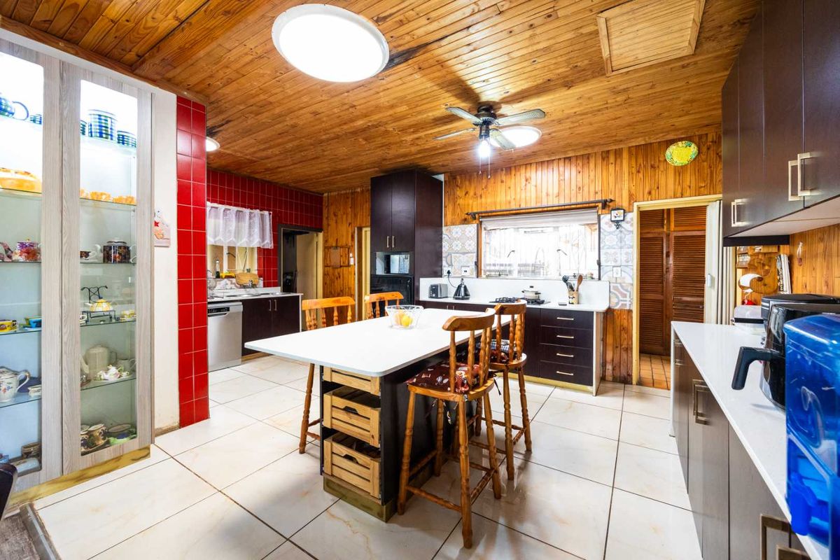 Spacious kitchen featuring a central island, tiled flooring, and extensive timber paneling on walls and ceilings, offering a functional layout with ample storage.