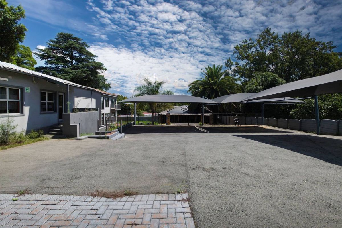 Exterior view of a business property featuring a paved parking area with multiple shade-cloth carports and building access.