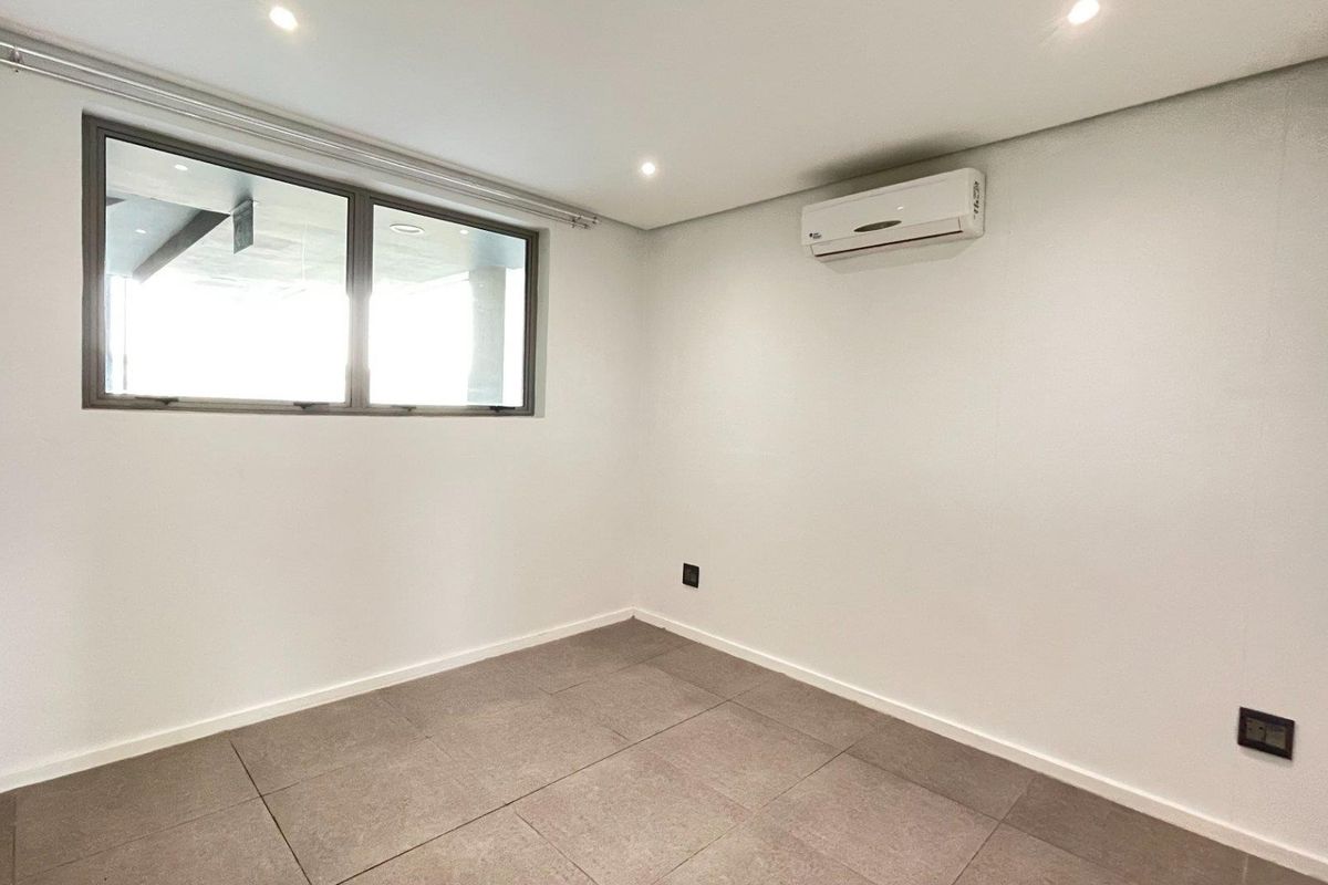 A clean, empty bedroom featuring tiled flooring, recessed downlighting, and a wall-mounted split-system air conditioning unit.