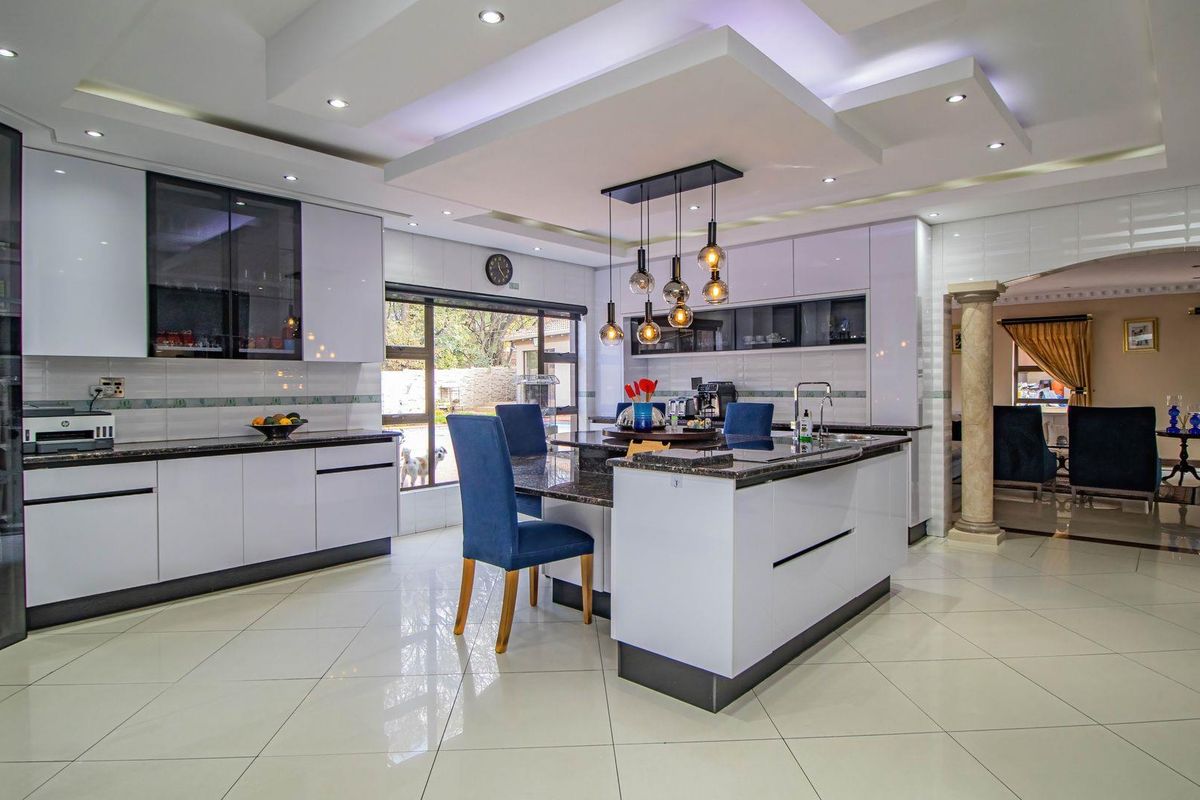 Modern kitchen featuring high-gloss cabinetry, a central island with integrated sink, granite countertops, and a sophisticated recessed ceiling with ambient lighting.