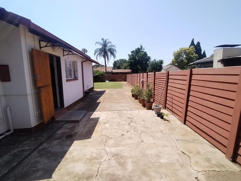 A rear exterior view showing a concrete driveway, a timber boundary fence, and access to the side of the house.