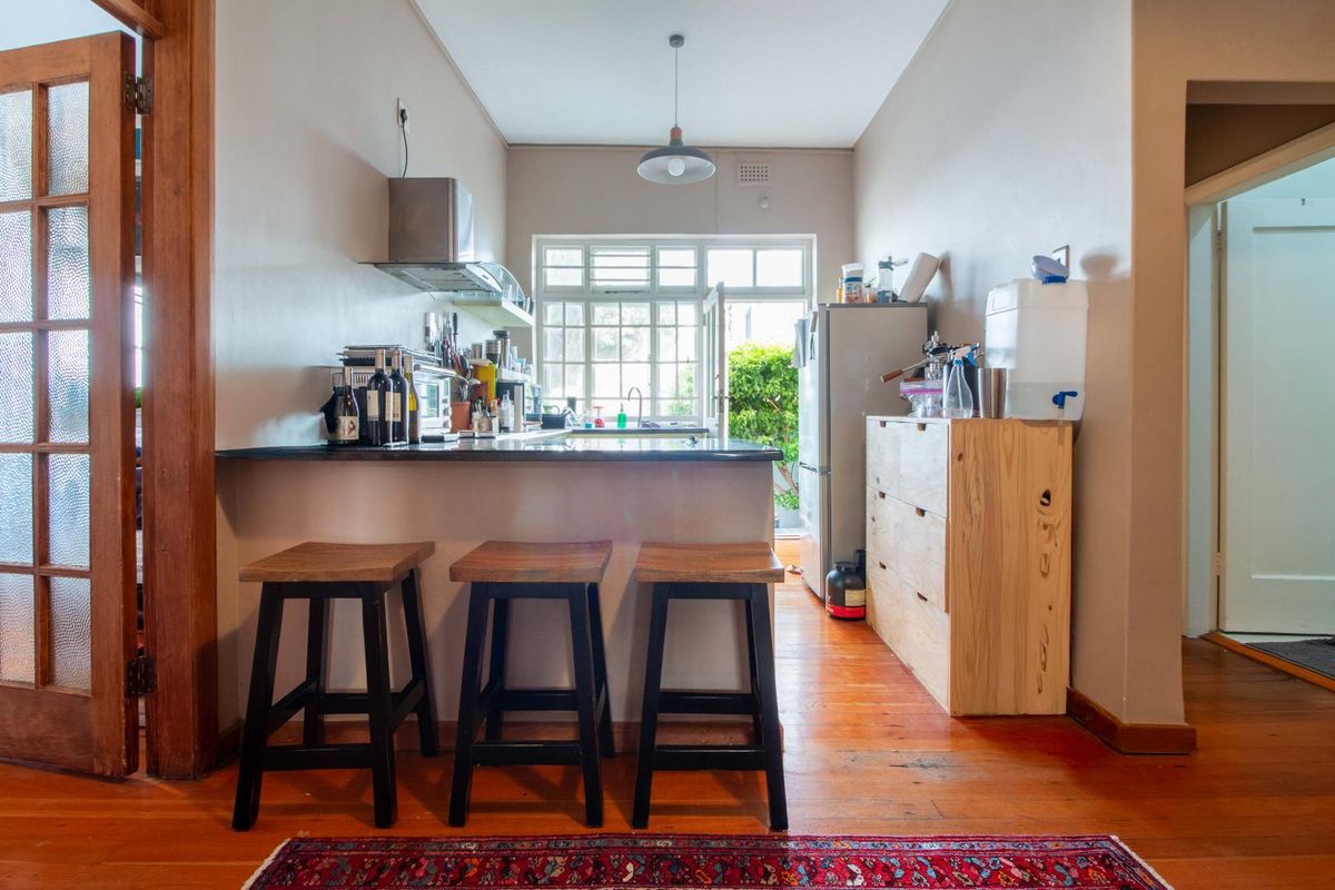 A functional kitchen featuring a breakfast bar, dark stone countertops, stainless steel extractor fan, and direct access to an outdoor area.