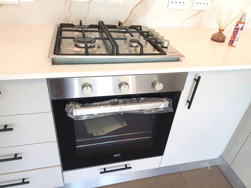 Modern kitchen featuring a stainless steel gas hob, built-in oven, stone countertops, and marble-look splashback with contemporary cabinetry.