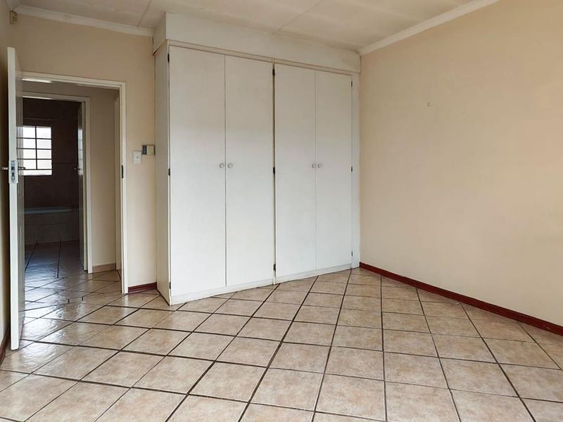 An empty bedroom featuring tiled flooring and built-in cupboards, with an adjacent view into a bathroom area.