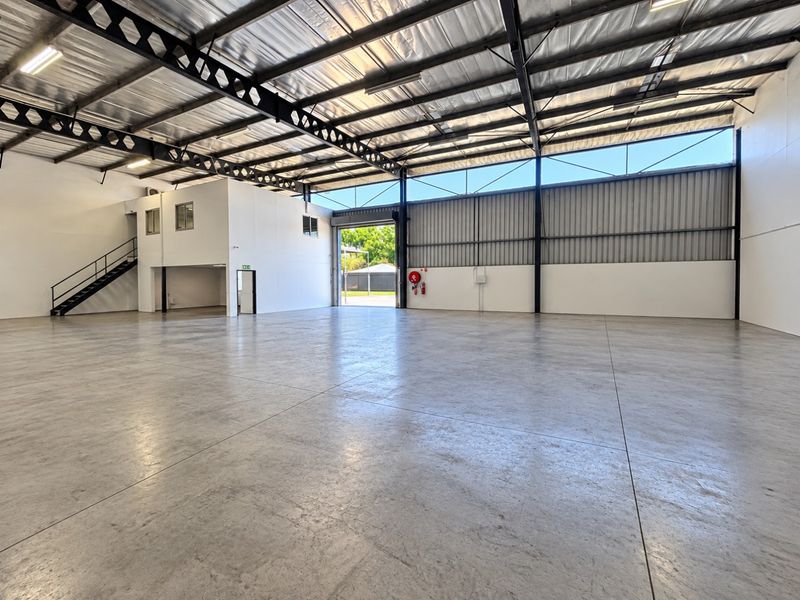 Spacious industrial warehouse featuring polished concrete flooring, high-clearance ceilings with exposed steel trusses, a mezzanine level, and large roller door access.