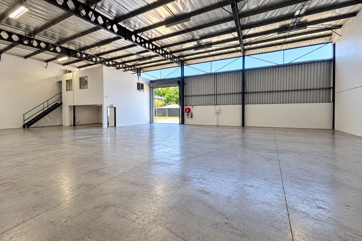 Spacious industrial warehouse featuring polished concrete flooring, high-clearance ceilings with exposed steel trusses, a mezzanine level, and large roller door access.