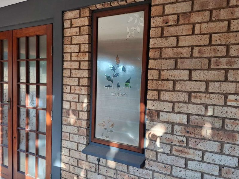 A covered patio area featuring exposed brick walls, a timber-framed glass door, and a decorative etched glass window.