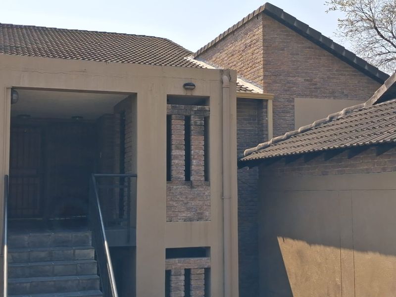 Exterior view of an apartment building entrance featuring brick masonry, tiled roofing, and a concrete staircase with a metal handrail.