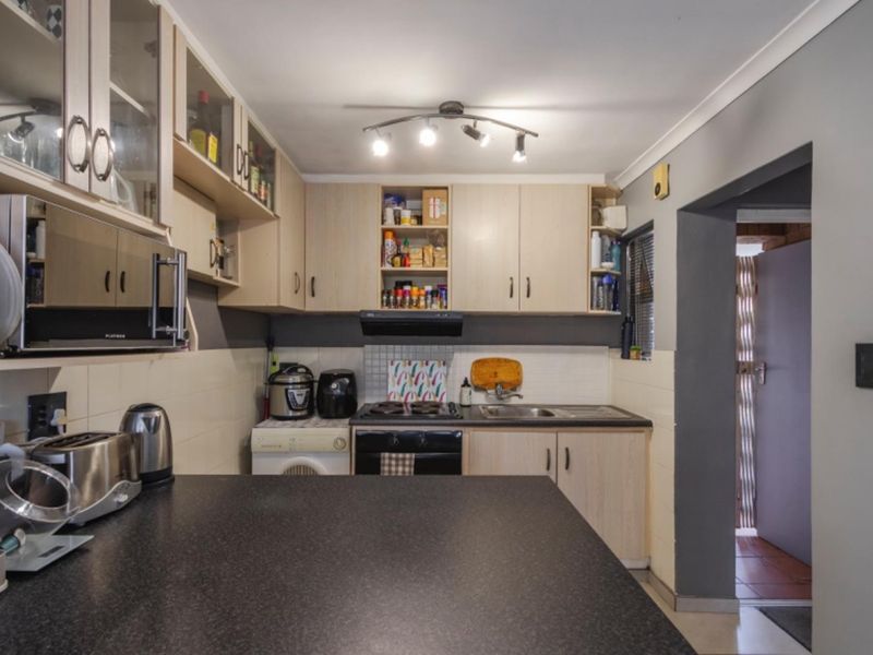 A functional kitchen featuring light wood-toned cabinetry, dark laminate countertops, a built-in oven with extractor fan, and a tiled backsplash.