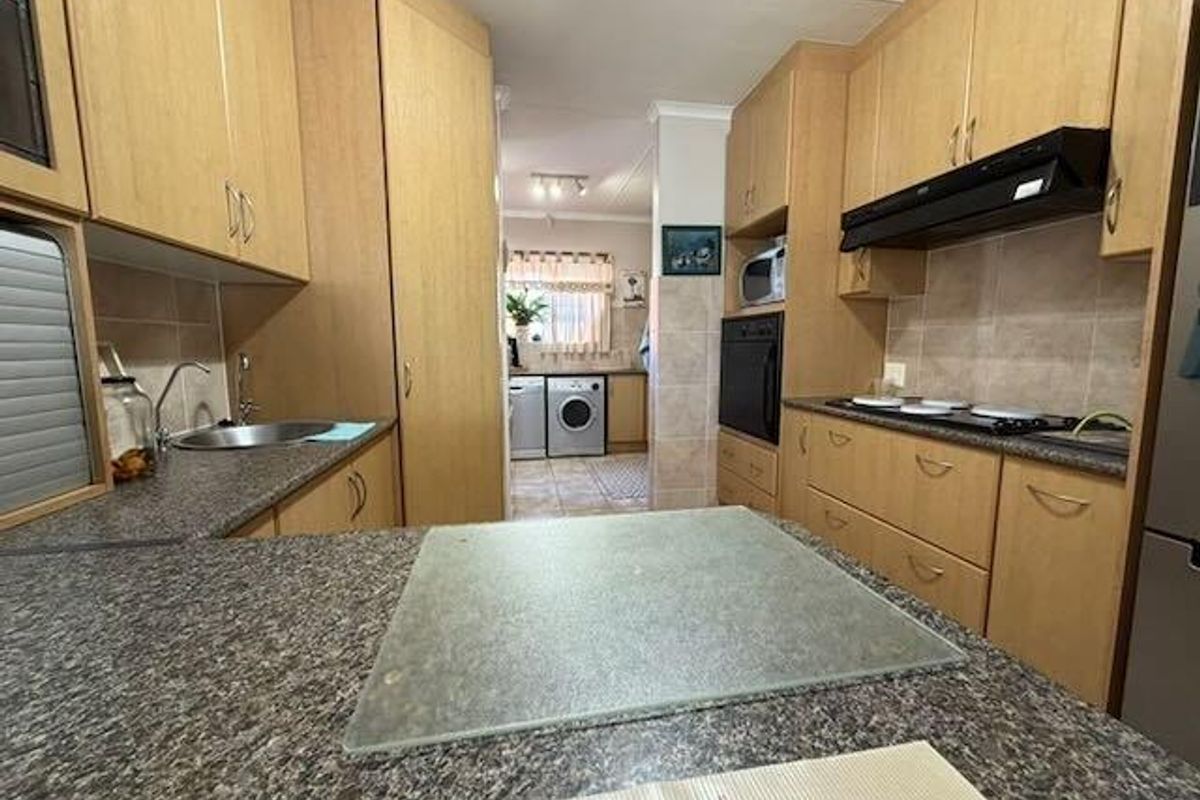 Functional kitchen featuring laminate cabinetry, built-in oven, electric hob, and a tiled backsplash, with an adjacent laundry area visible in the background.