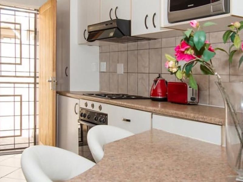 Compact kitchen featuring built-in cabinetry, laminate countertops, integrated oven and hob, tiled backsplash, and direct access to an exterior security gate.