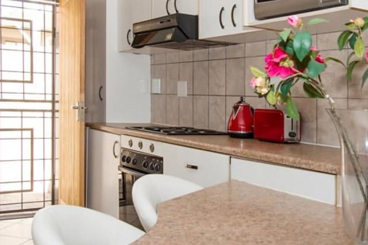 Compact kitchen featuring built-in cabinetry, laminate countertops, integrated oven and hob, tiled backsplash, and direct access to an exterior security gate.