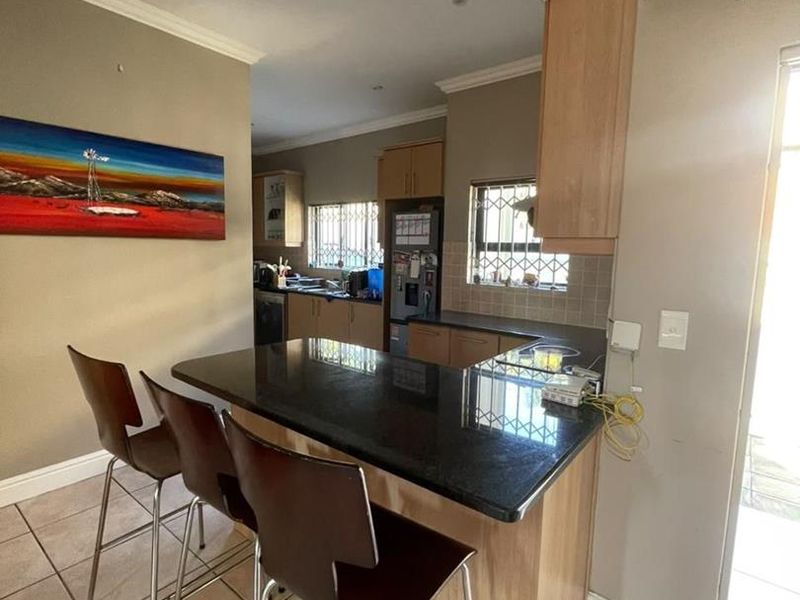 A functional kitchen featuring granite countertops, wooden cabinetry, tiled flooring, and a breakfast bar area with direct access to the exterior.