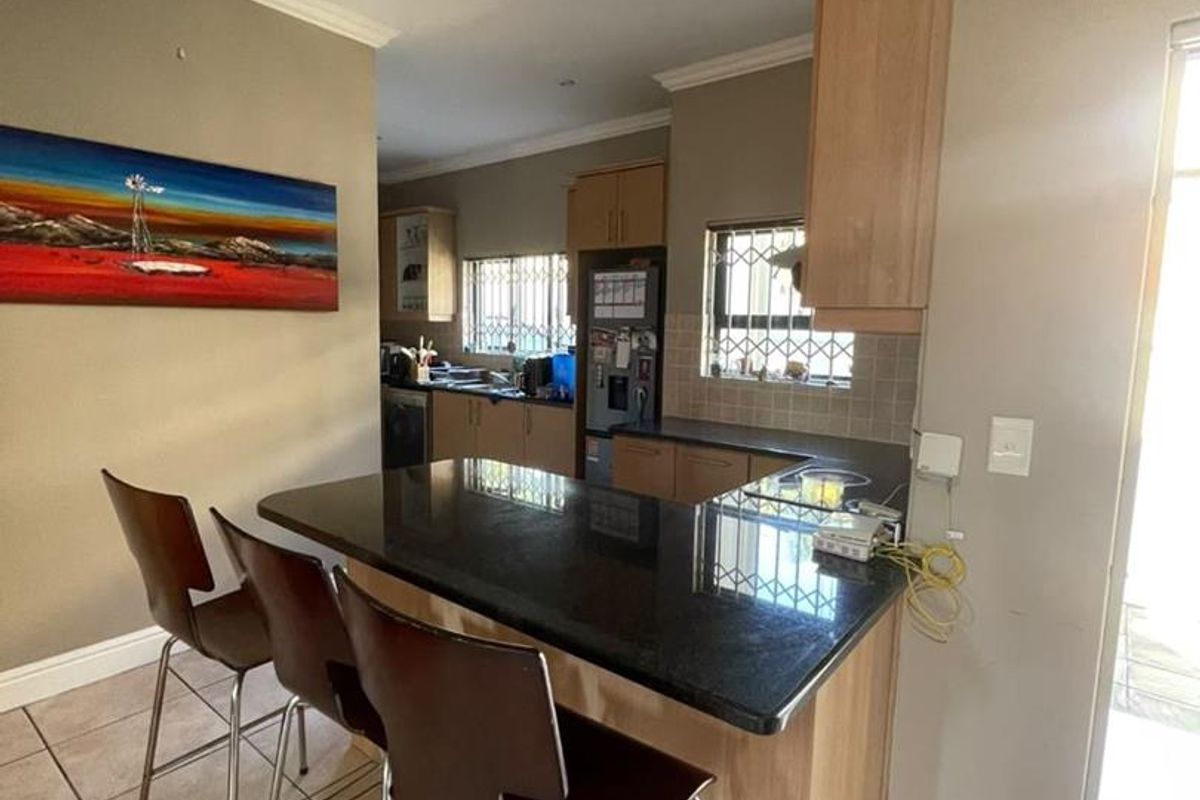 A functional kitchen featuring granite countertops, wooden cabinetry, tiled flooring, and a breakfast bar area with direct access to the exterior.