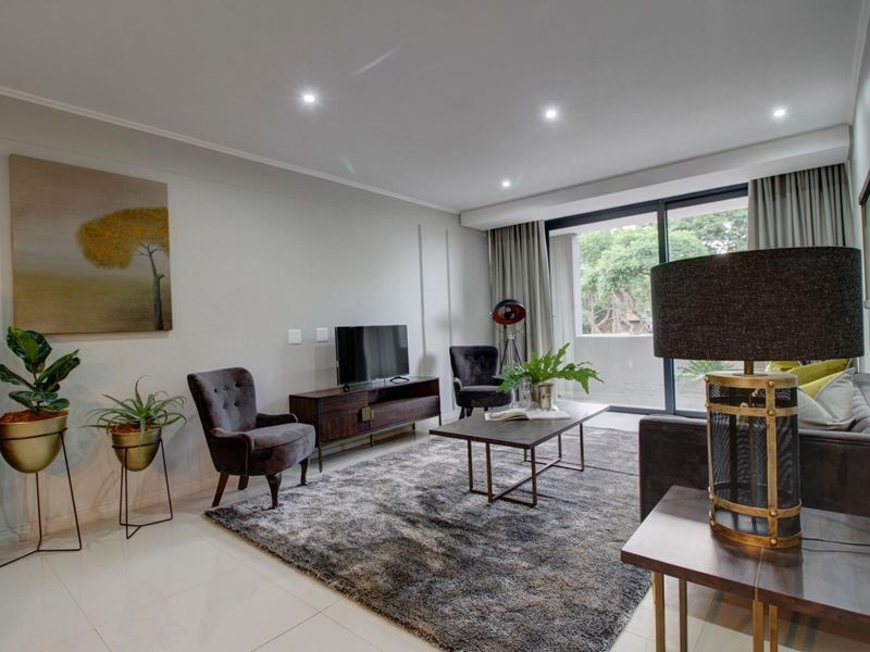 A well-maintained living room featuring modern recessed downlighting, large sliding glass doors leading to a balcony, and clean tiled flooring.