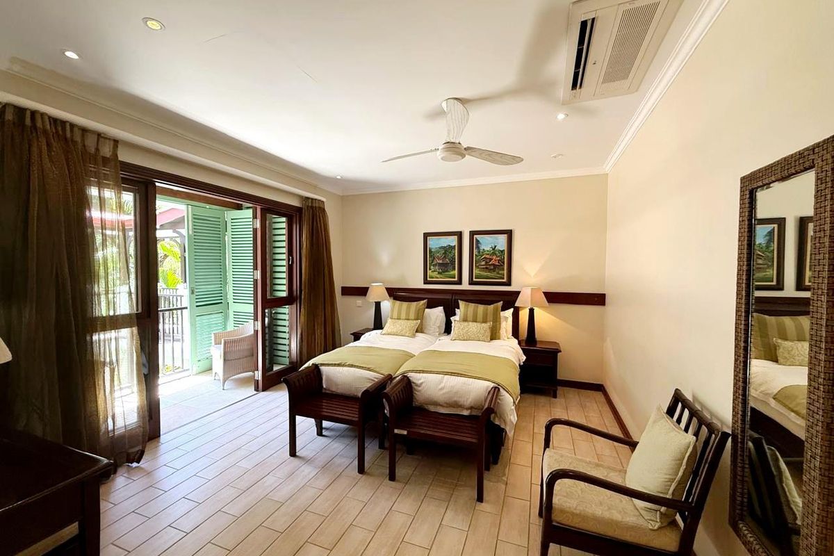 A well-maintained bedroom featuring tiled flooring, a ceiling fan, and integrated air conditioning, with direct access to a private balcony through sliding doors.
