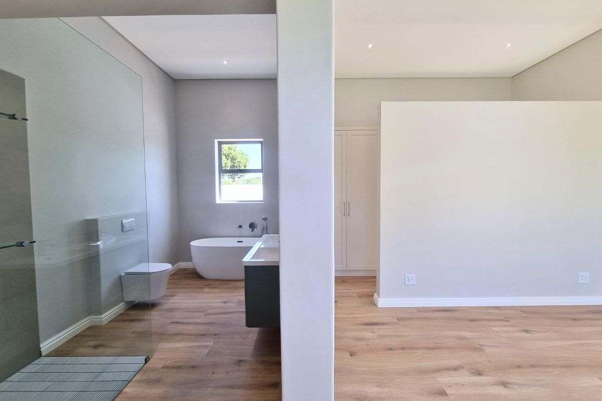 Modern open-plan bedroom and en-suite bathroom featuring a freestanding bathtub, glass-enclosed shower, wall-mounted toilet, and built-in cabinetry with light wood-look flooring.