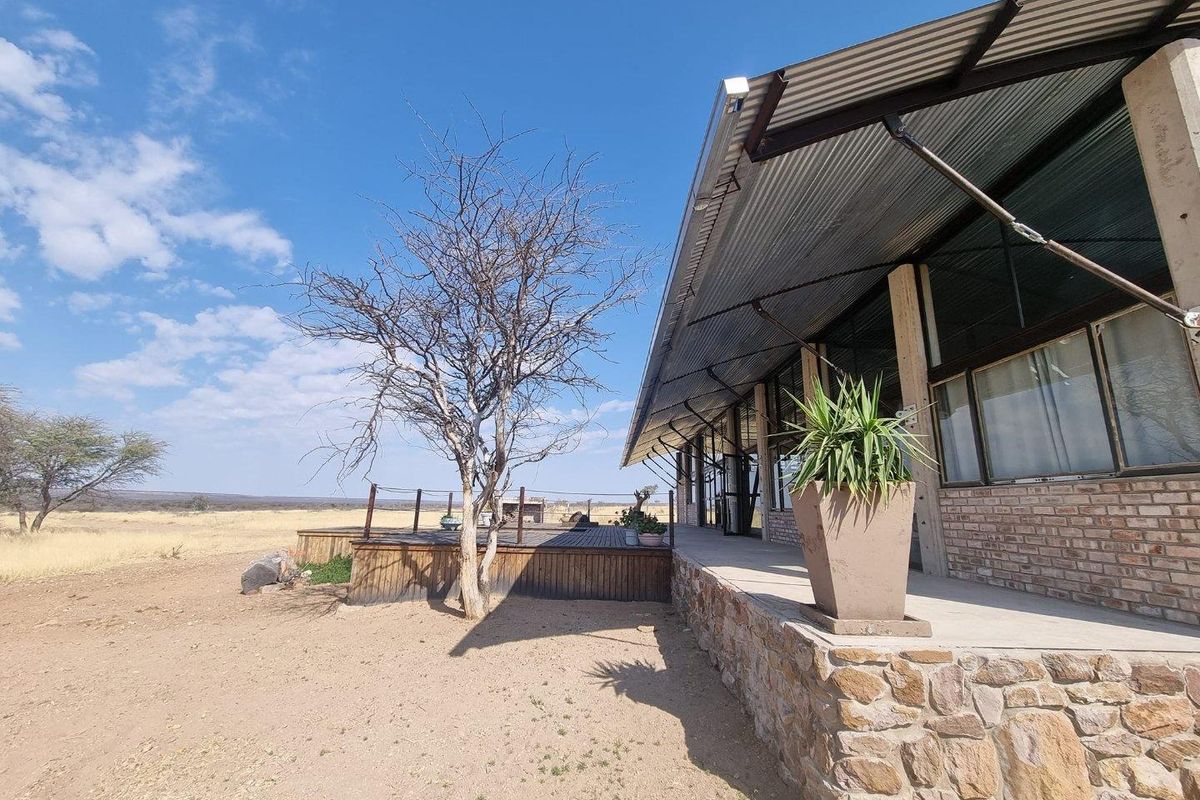 Exterior view of a rustic building featuring a stone base, corrugated metal roof, and an attached wooden deck overlooking a dry landscape.