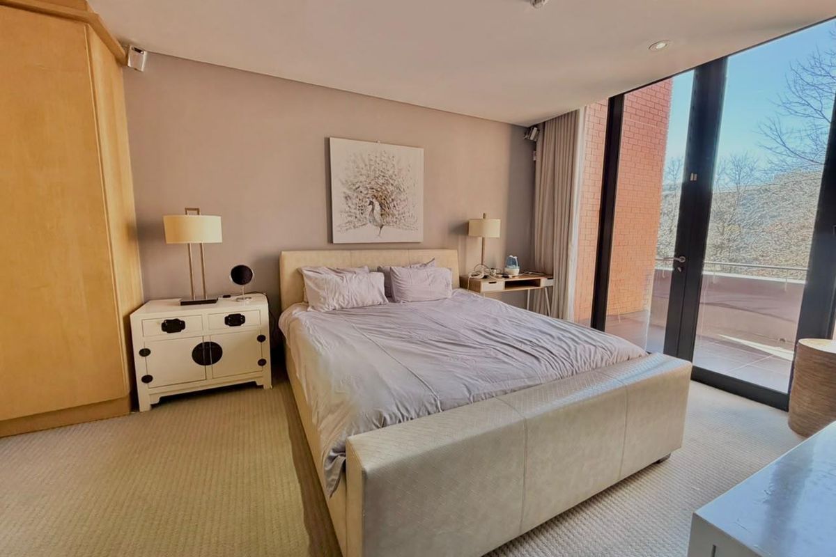 Spacious bedroom featuring built-in wooden cabinetry, neutral carpeting, and large floor-to-ceiling glass doors providing direct access to a private balcony.