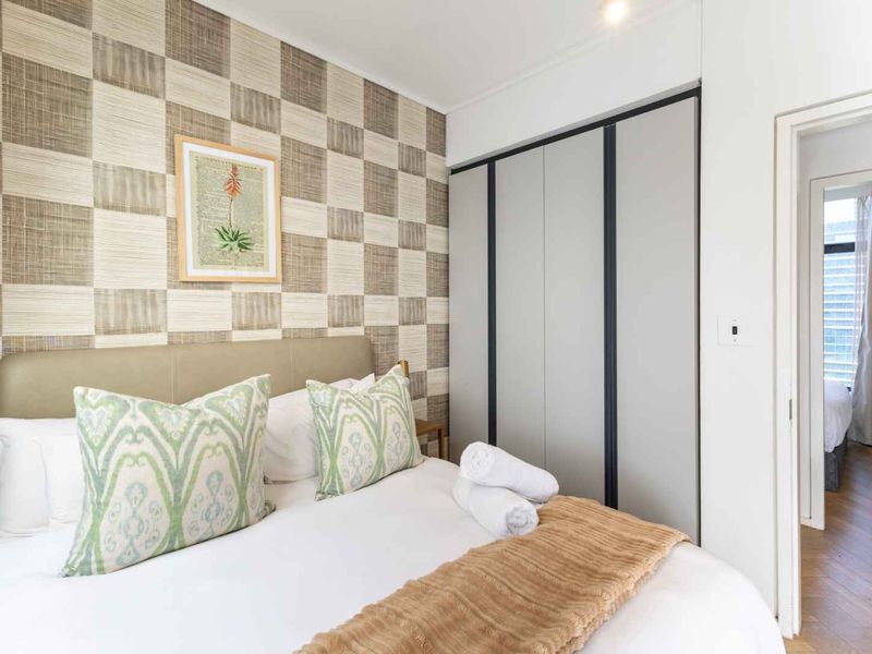 A well-maintained bedroom featuring built-in wardrobes, modern wallpaper, and hardwood flooring, with an adjoining hallway view.