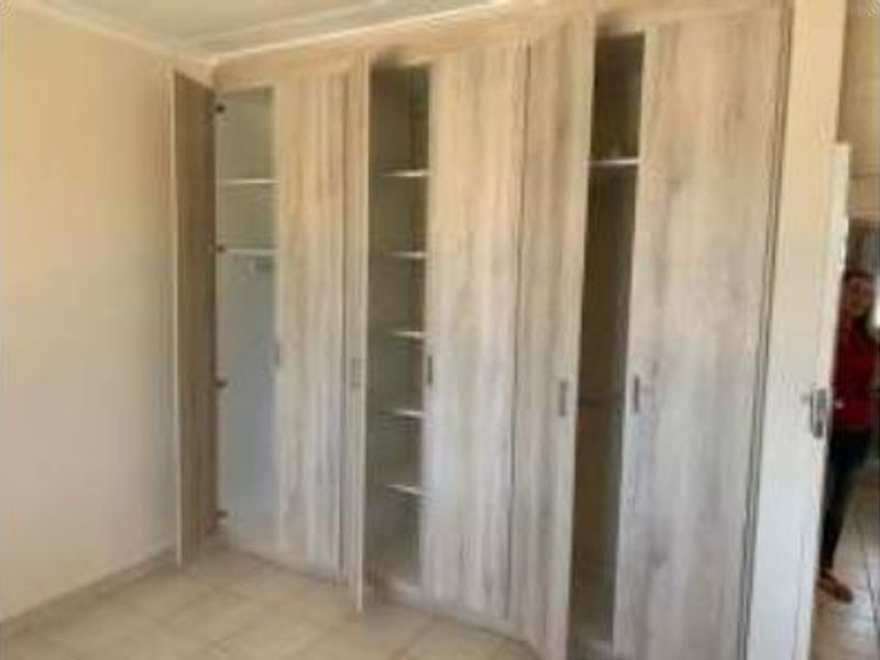 A bedroom featuring light wood-finish built-in cupboards and neutral tiled flooring, offering ample storage space.