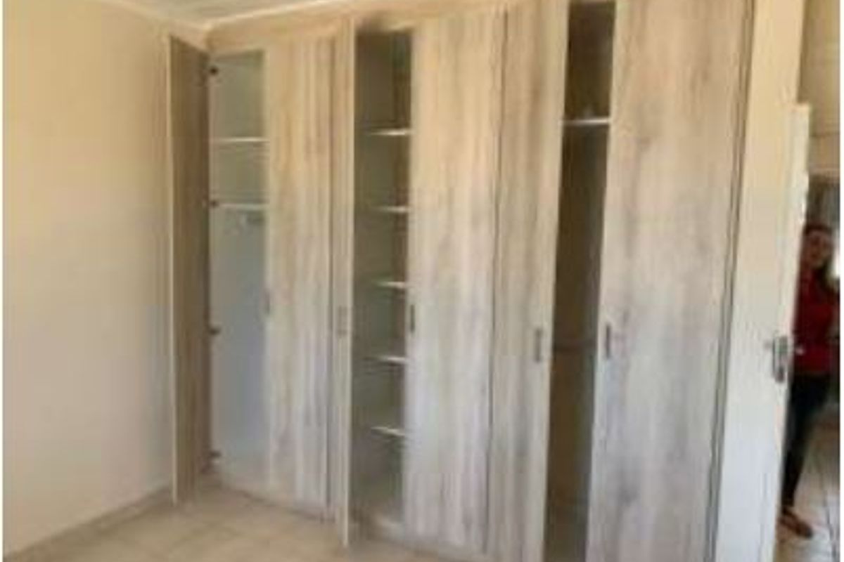 A bedroom featuring light wood-finish built-in cupboards and neutral tiled flooring, offering ample storage space.