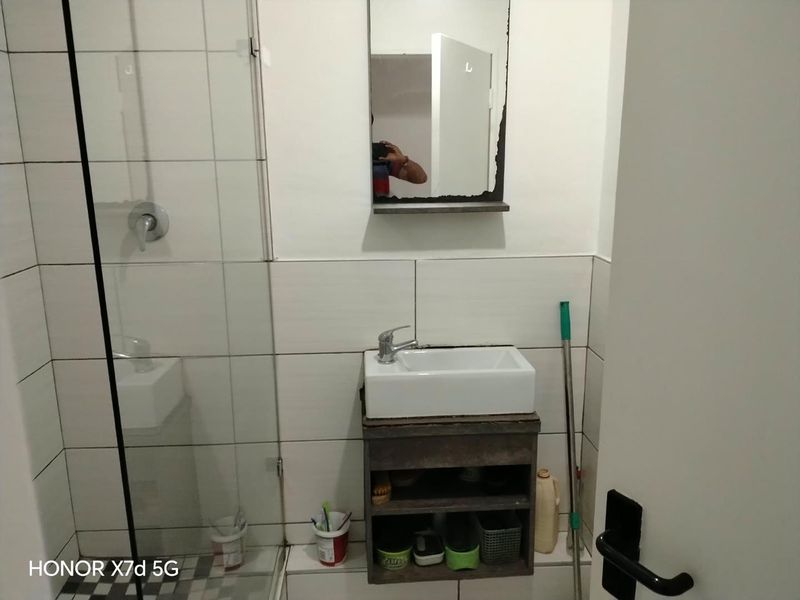 Compact bathroom featuring a shower enclosure, wall-mounted vanity with basin, and tiled walls. The space is functional but shows signs of wear.