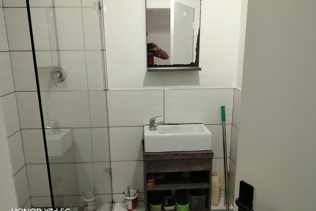 Compact bathroom featuring a shower enclosure, wall-mounted vanity with basin, and tiled walls. The space is functional but shows signs of wear.