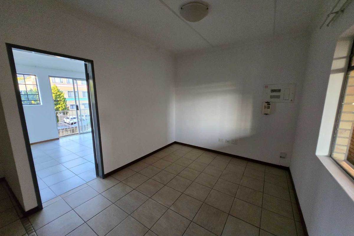 An empty, neutrally finished living area featuring tiled flooring, an intercom system, and an electrical distribution board, with access to an adjacent balcony.