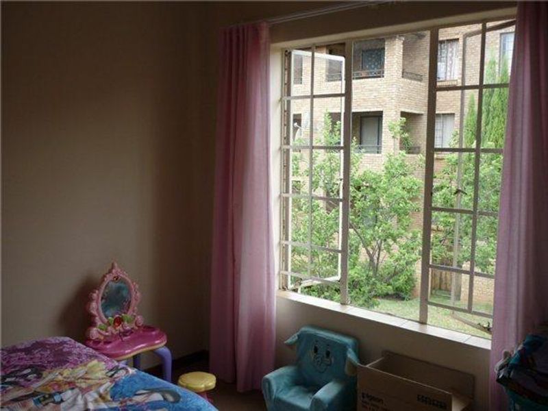 A bedroom featuring a large steel-framed casement window with views of the surrounding apartment complex and greenery.