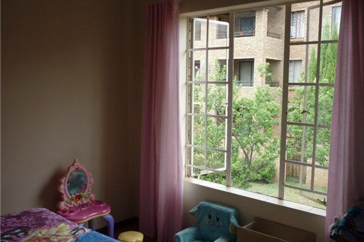 A bedroom featuring a large steel-framed casement window with views of the surrounding apartment complex and greenery.