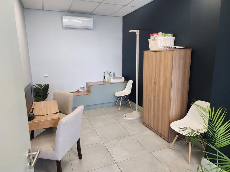 A professional office space featuring tiled flooring, a suspended ceiling, built-in cabinetry with an integrated sink, and a wall-mounted air conditioning unit.