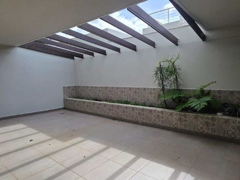 A spacious outdoor patio featuring a modern pergola roof structure and a decorative tiled built-in planter box.